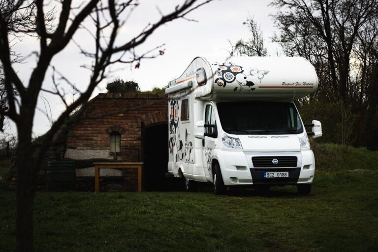 carado - A white Fiat camper parked near a rustic brick shed in a rural landscape.